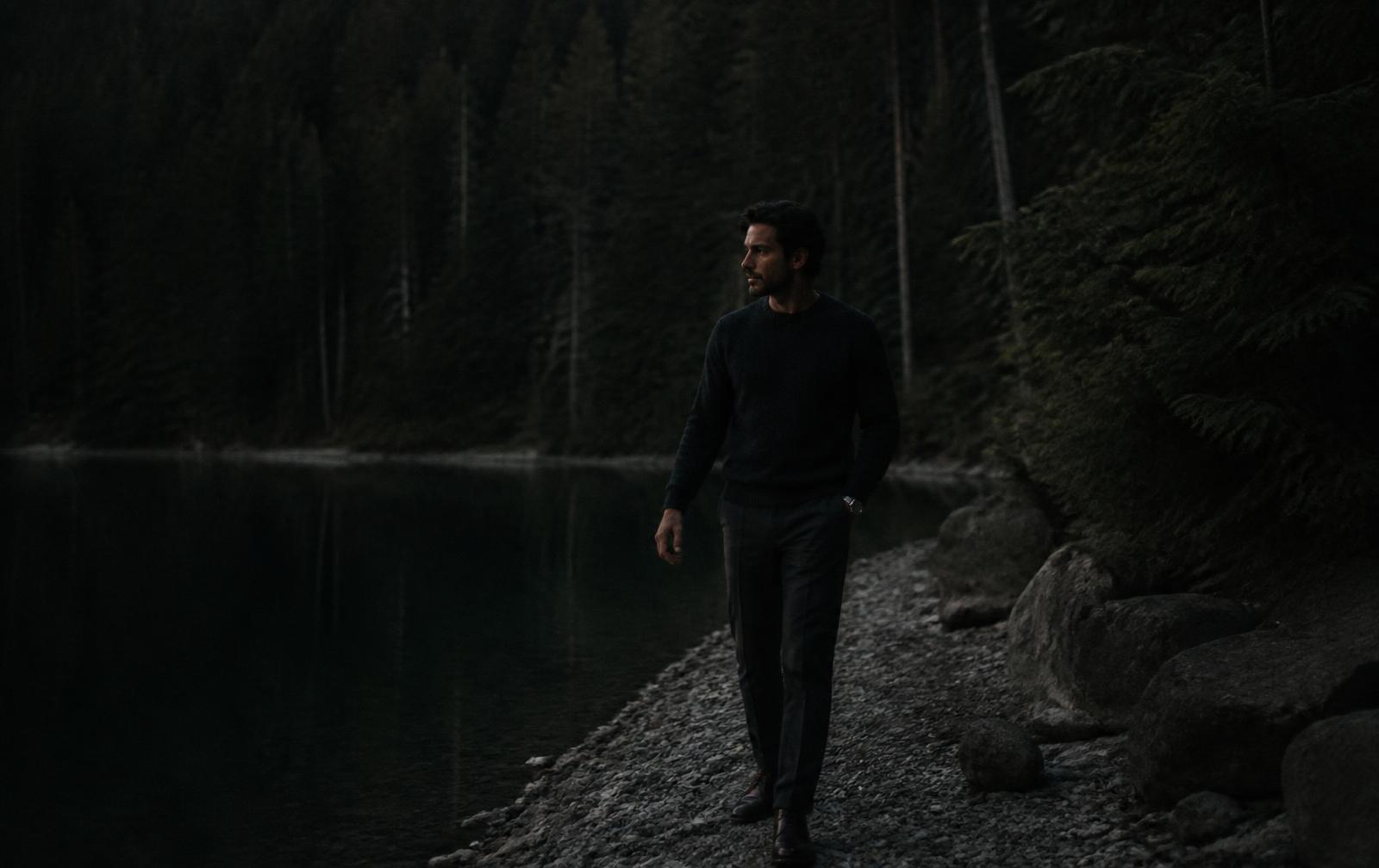 A man walking alone at dusk beside a quiet forest lake